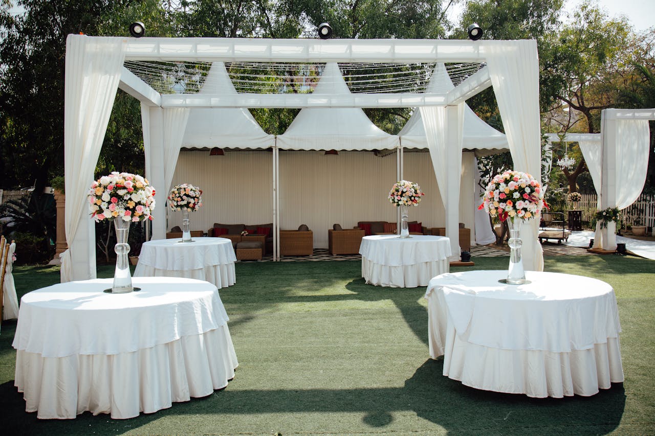 Charming outdoor wedding setup with white draped pergolas and floral centerpieces under a sunny sky.